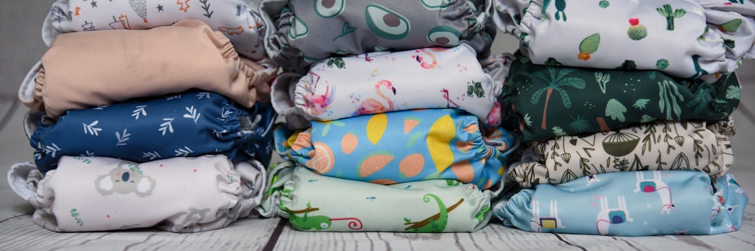 : A horizontal banner image showing three stacks of folded, colorful cloth diapers with various patterns, including koalas, flamingos, avocados, and tropical plants.