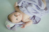 Adorable baby wrapped in a light purple hooded towel with an animal face design, lying on a soft surface